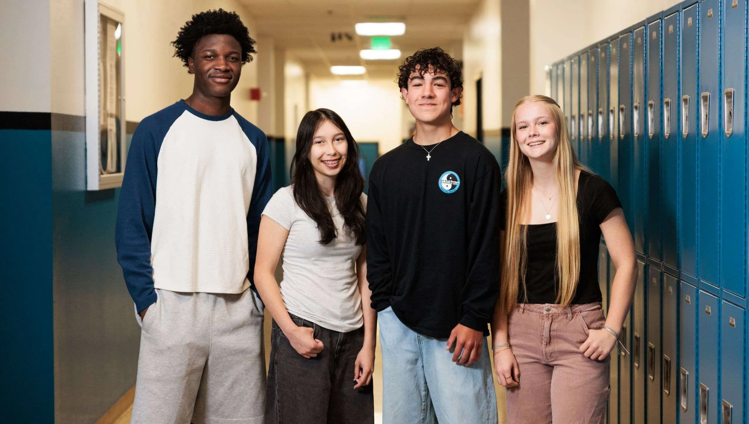 Four smiling high school students stand together in a school hallway