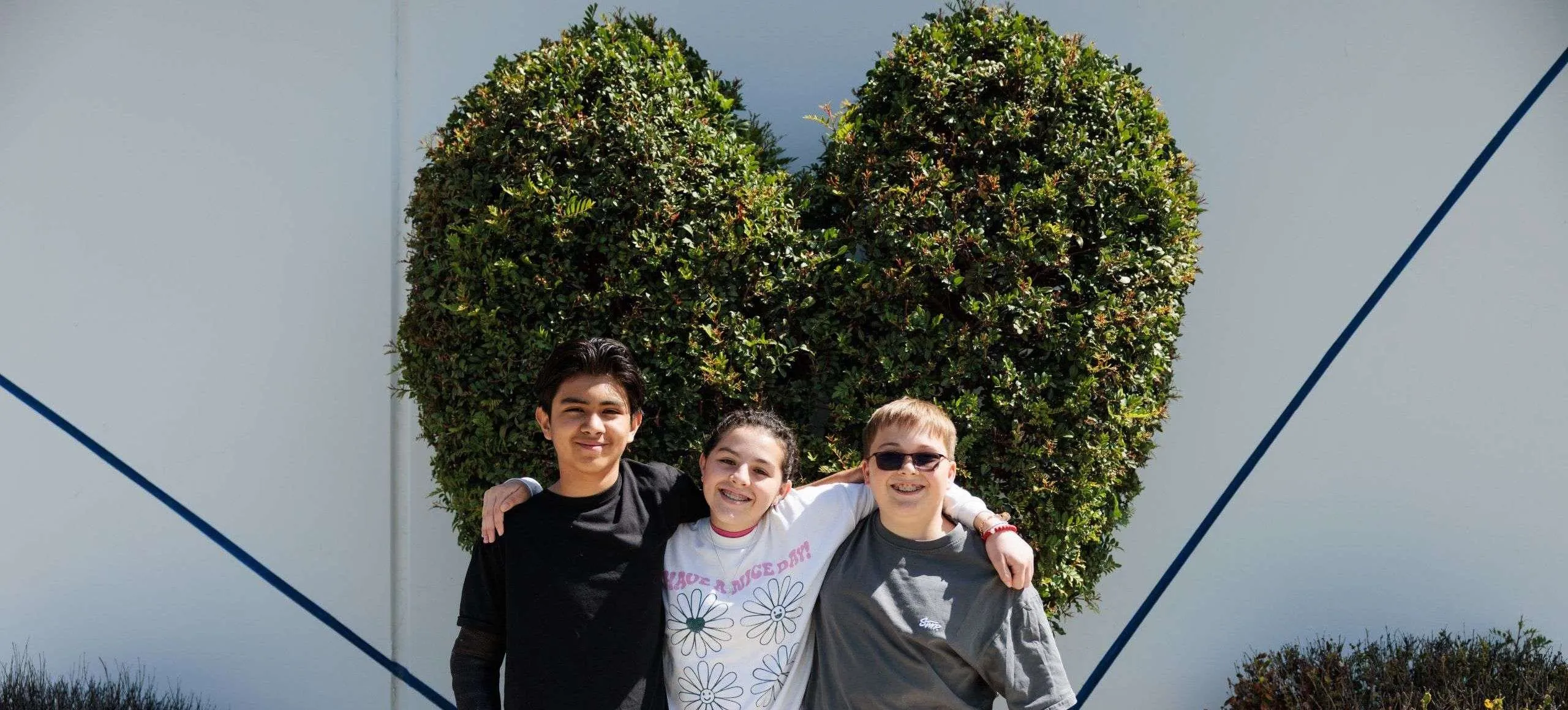 Students by the Heart-Shaped Hedge Three junior high students pose in front of a heart-shaped hedge on campus